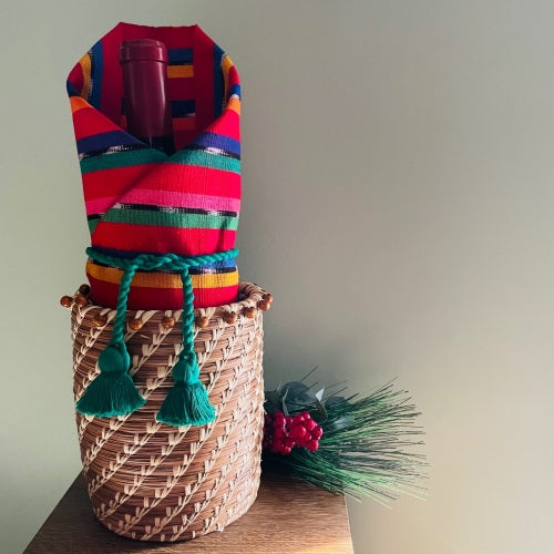 Wine bottle, gift wrapped in placemat and fastened in Christmas Green napkin cord, placed in pine needle Julia Basket